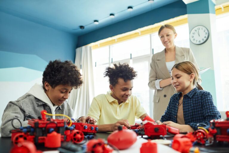 Smiling students collaborating on a robotics project under teacher's guidance in a classroom setting.